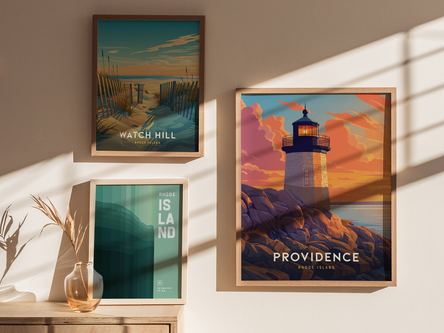Three framed posters are displayed on a wall, featuring scenic views of Rhode Island, including a lighthouse at sunset, a coastal path, and minimalist text design.