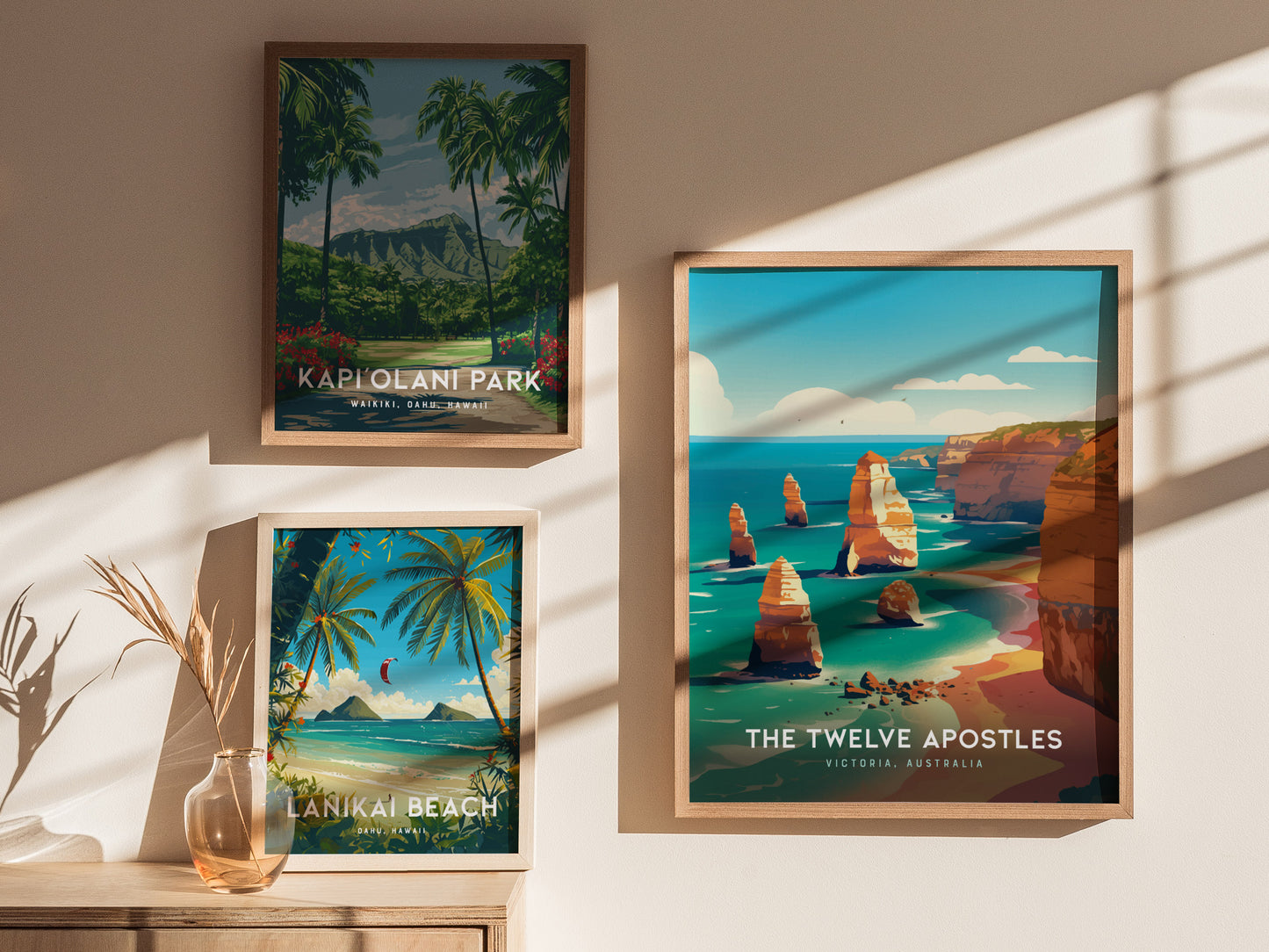 Three framed posters are displayed on a wall, featuring Kapiolani Park, Lanikai Beach, and the Twelve Apostles with vibrant illustrations of each location. Sunlight casts shadows across them.