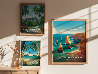 Three framed posters are displayed on a wall, featuring Kapiolani Park, Lanikai Beach, and the Twelve Apostles with vibrant illustrations of each location. Sunlight casts shadows across them.