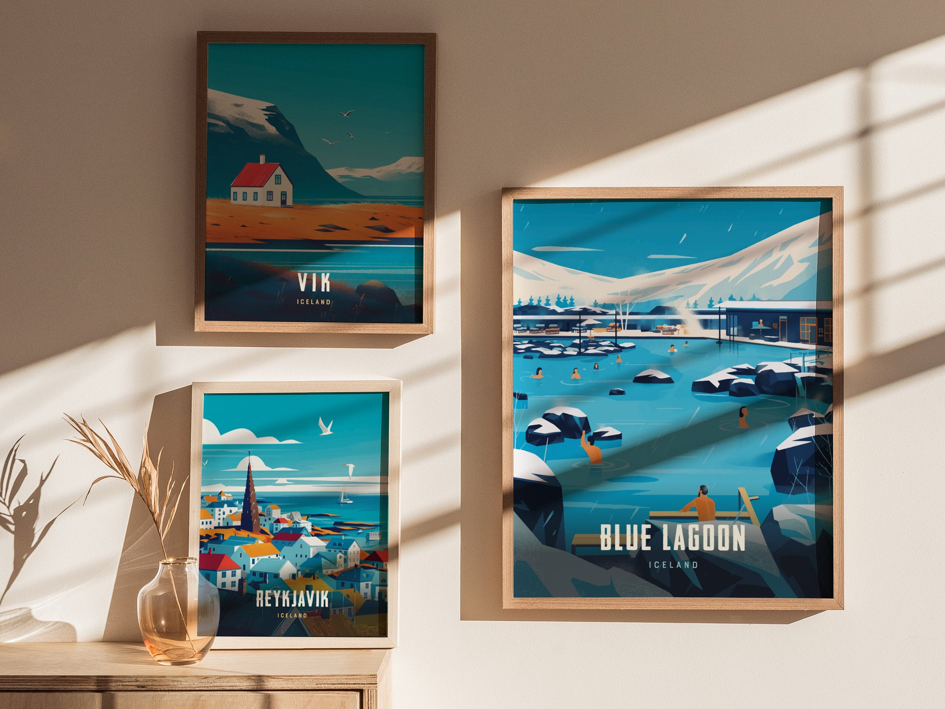 Three framed posters on a sunlit wall depict Icelandic landscapes: a Blue Lagoon scene, a colorful Reykjavik skyline, and a solitary house in Vik.