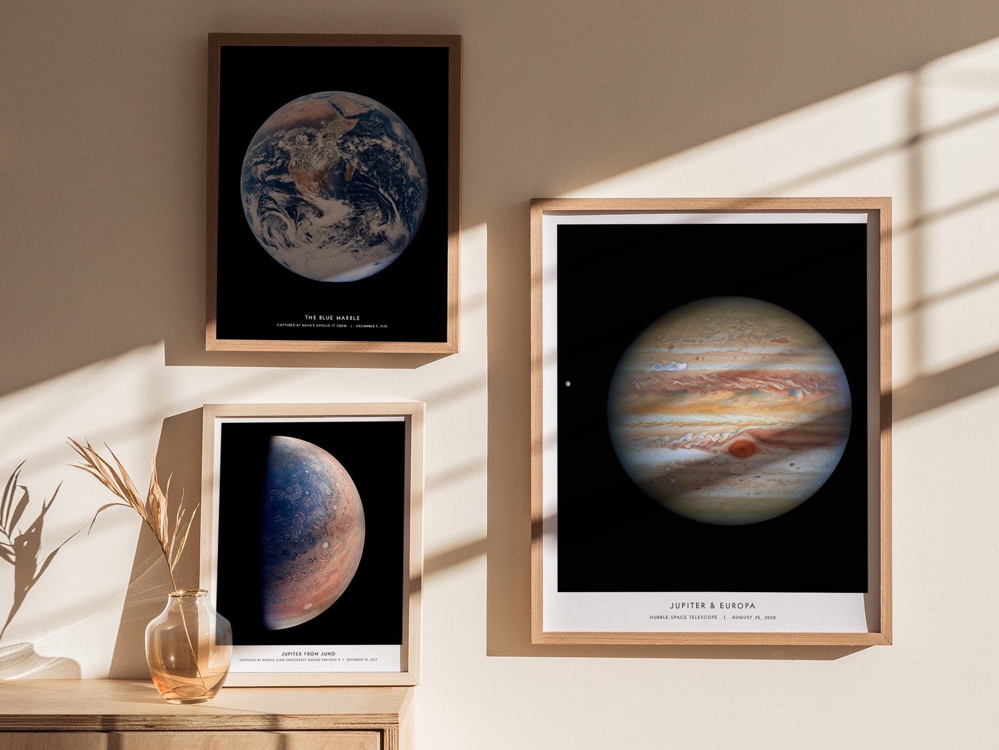 Framed posters of Earth, Mars, and Jupiter on a wall with sunlight casting shadows.
