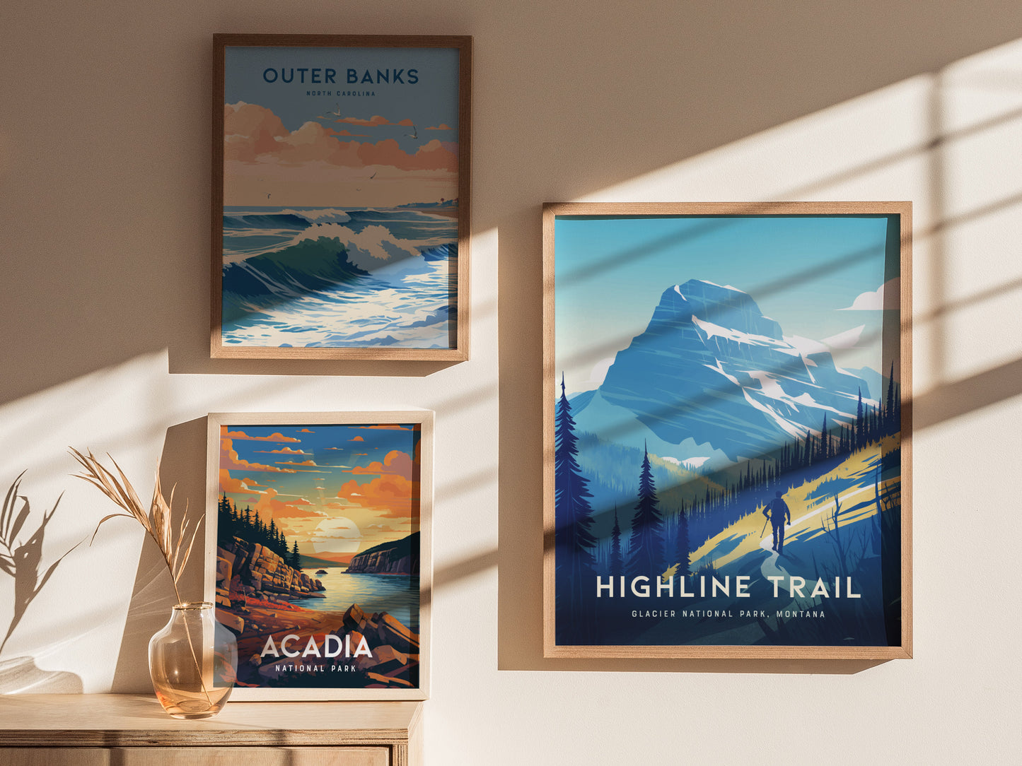 Three framed posters are displayed on a sunlit wall, featuring scenic landscapes of Outer Banks, Acadia National Park, and the Highline Trail in Glacier National Park.