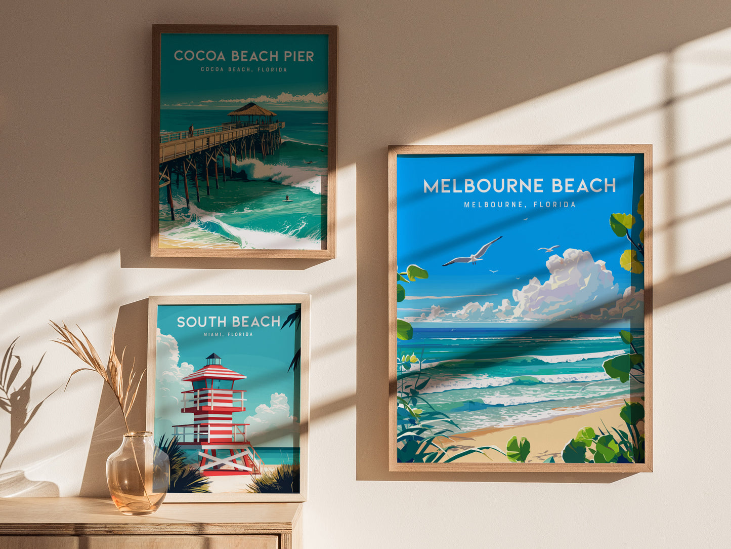 Three framed beach posters are displayed on a sunlit wall, featuring Cocoa Beach Pier, South Beach with a lifeguard tower, and Melbourne Beach with seagulls and ocean waves.