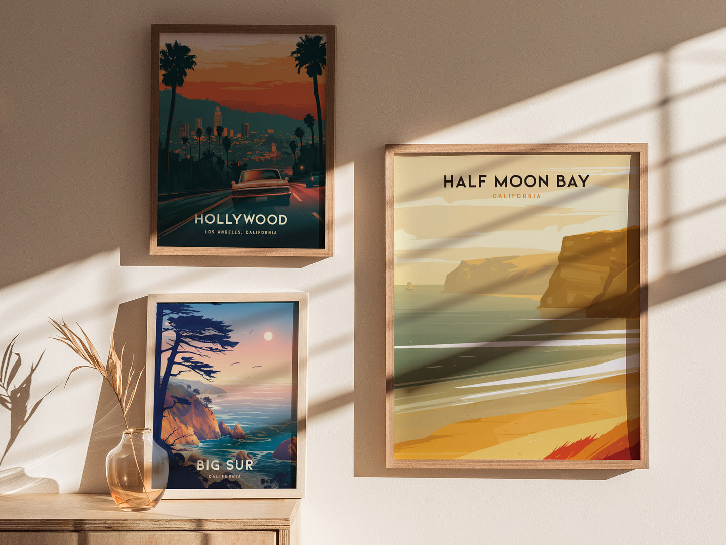 Three framed posters are displayed on a sunlit wall: Hollywood with a cityscape, Half Moon Bay with coastal cliffs, and Big Sur depicting ocean waves and a sunset.