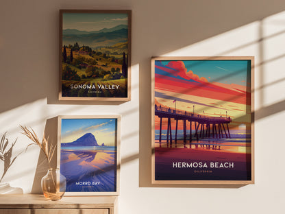 Three framed posters hang on a wall, showcasing Hermosa Beach, Sonoma Valley, and Morro Bay landscapes. Sunlight casts shadows, highlighting the vibrant colors and scenic designs.