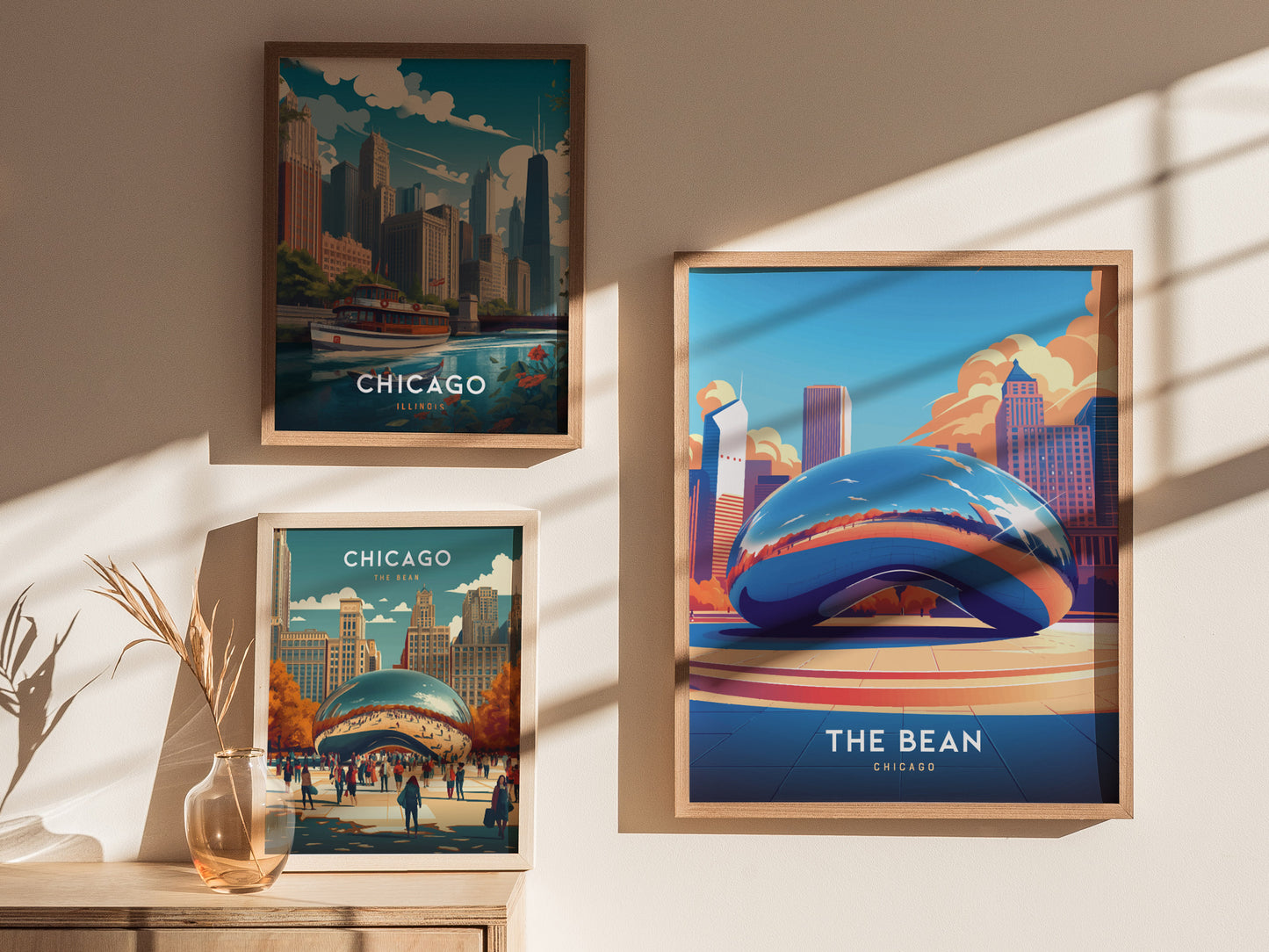 Three framed posters on a wall depict Chicago scenes, including a vibrant illustration of Cloud Gate. A decorative vase with dried grass is placed on a wooden surface below.