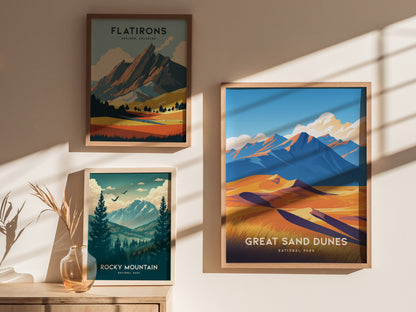 Three framed posters hang on a wall, displaying colorful landscapes of Flatirons, Rocky Mountain, and Great Sand Dunes National Park, illuminated by soft sunlight.