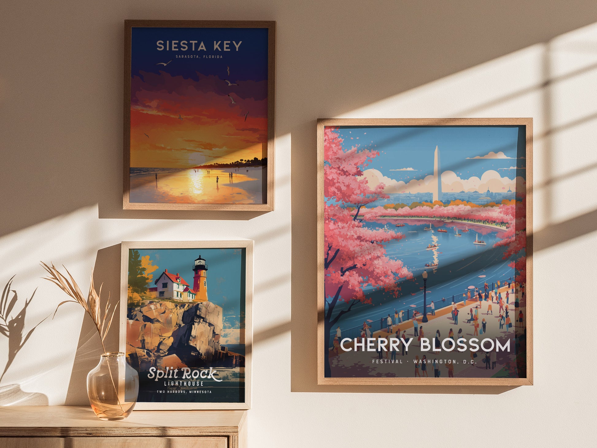 Three framed posters are displayed on a sunlit wall. The largest features cherry blossoms by the Washington Monument, another shows a sunset at Siesta Key, and the third depicts Split Rock Lighthouse on a rocky cliff.