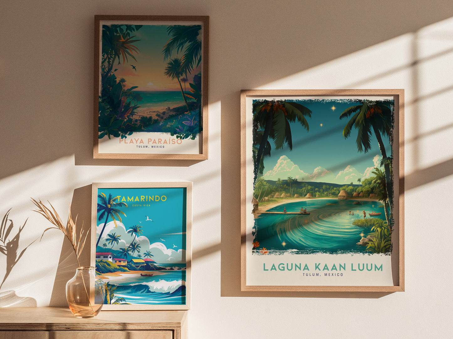 Three framed posters depicting tropical landscapes hang on a sunlit wall. The Laguna Kaan Luum poster shows a lagoon with palm trees and a serene atmosphere.