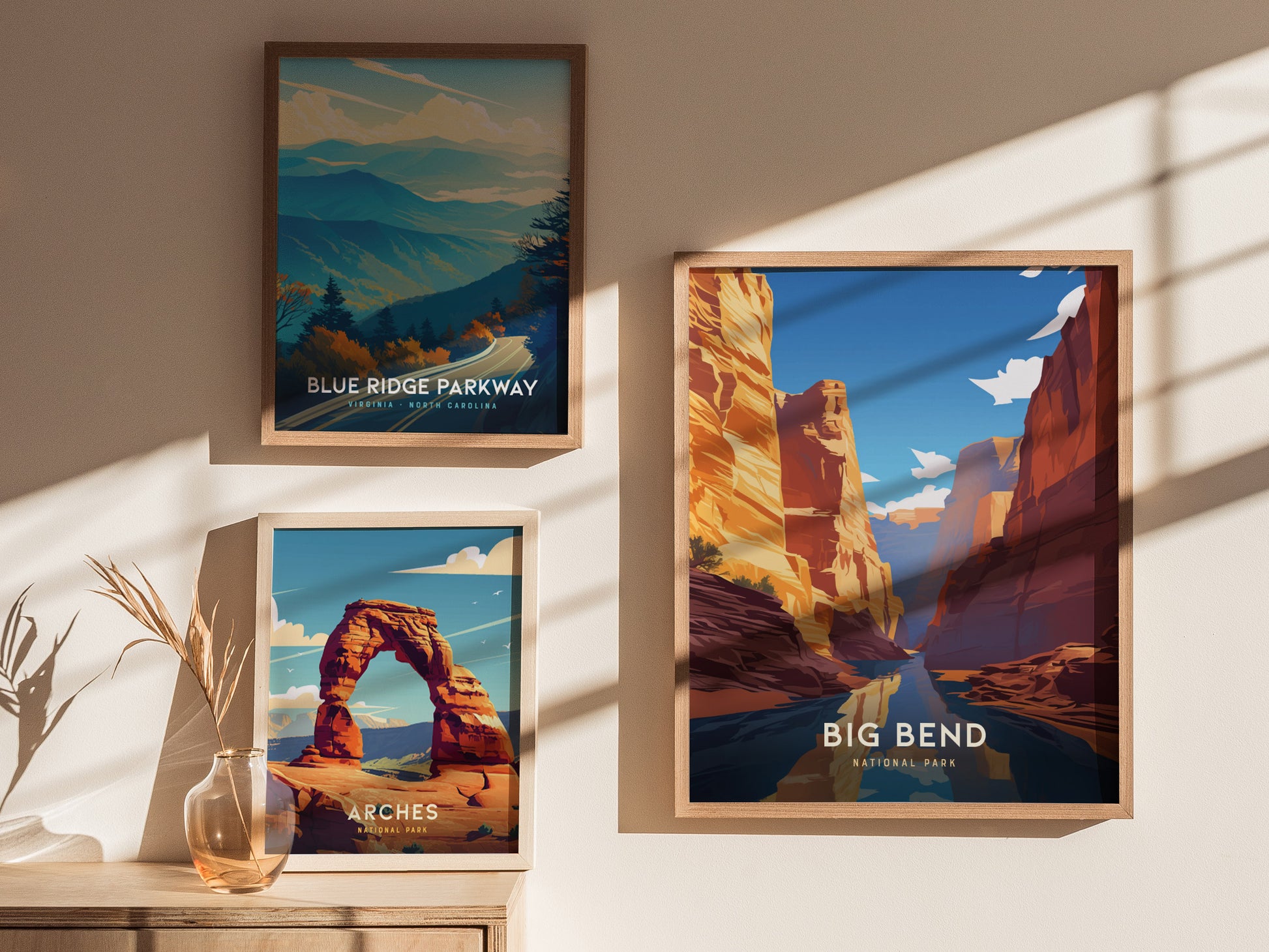 Three framed posters hang on a wall, depicting landscapes of Blue Ridge Parkway, Arches National Park, and Big Bend National Park, with sunlight casting shadows.