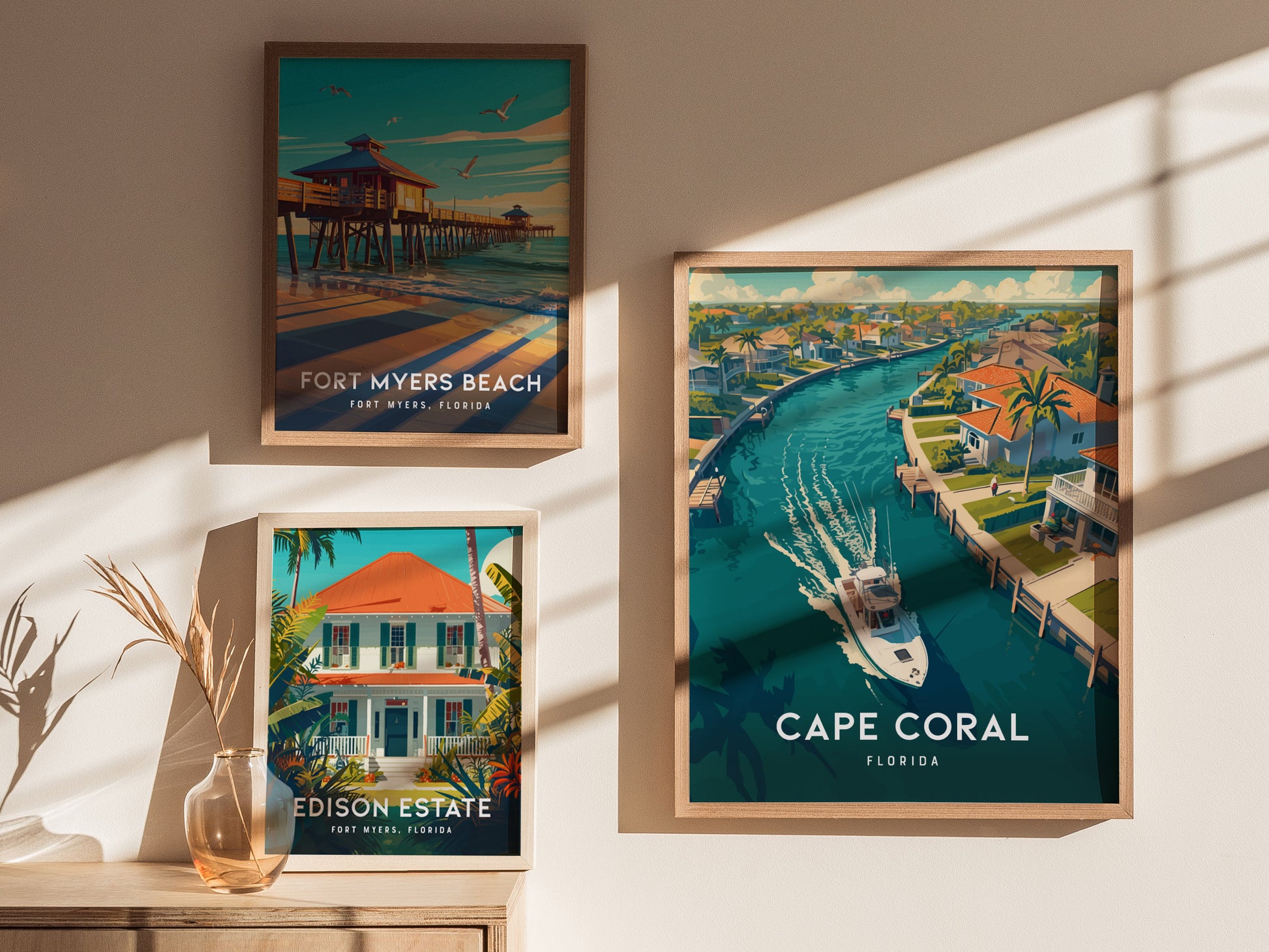 Three framed posters are displayed on a wall, featuring Cape Coral, Fort Myers Beach, and Edison Estate, with sunlight casting shadows across them. A vase with dried plants sits nearby.