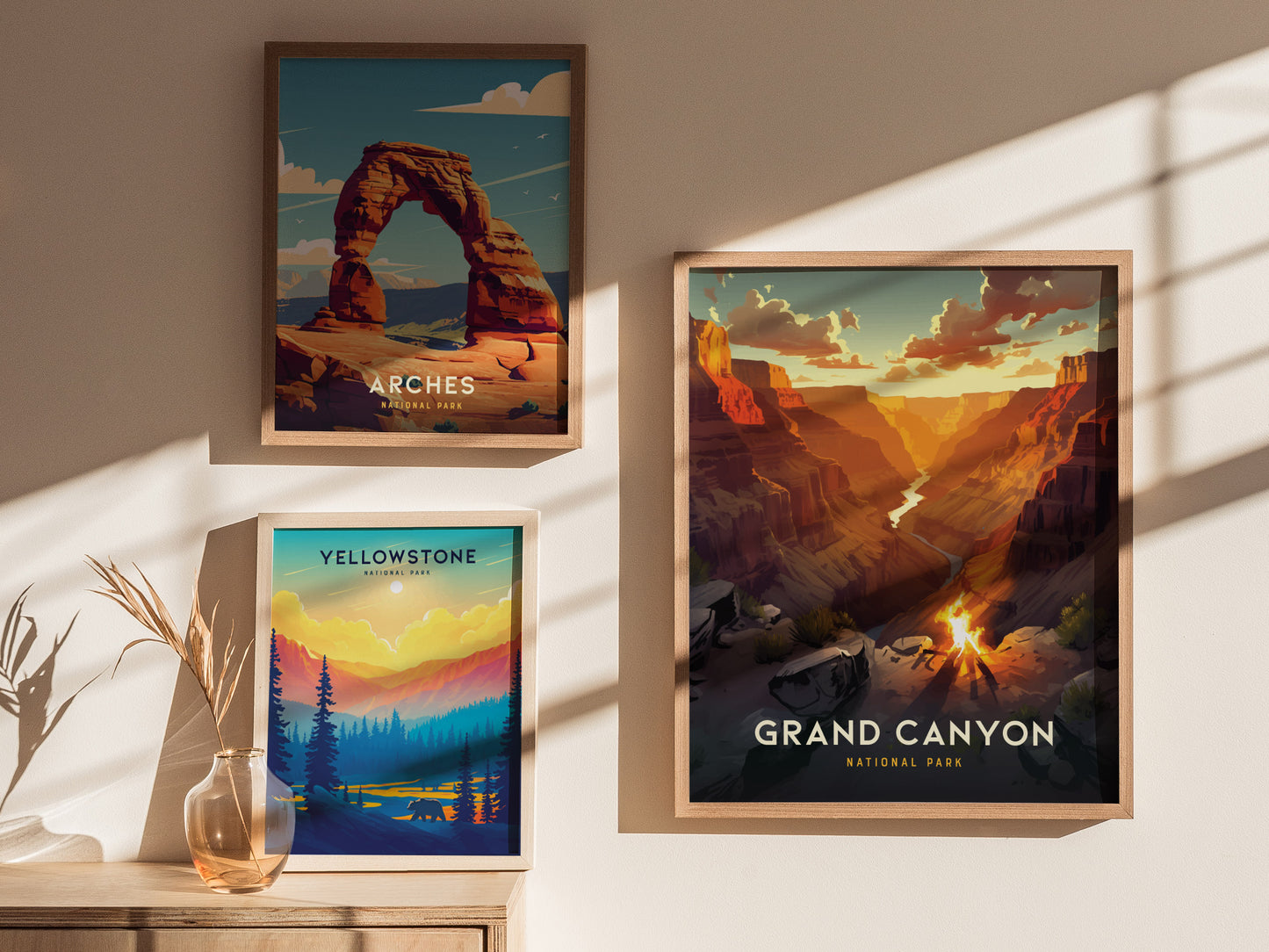 Three framed posters of national parks—Arches, Yellowstone, and Grand Canyon—are displayed on a sunlit wall, accompanied by a glass vase with dried plants on a wooden table.