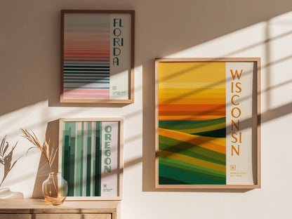 Three framed minimalist posters are displayed on a wall, each representing Florida, Oregon, and Wisconsin with abstract patterns in shades of green, gold, and pink.