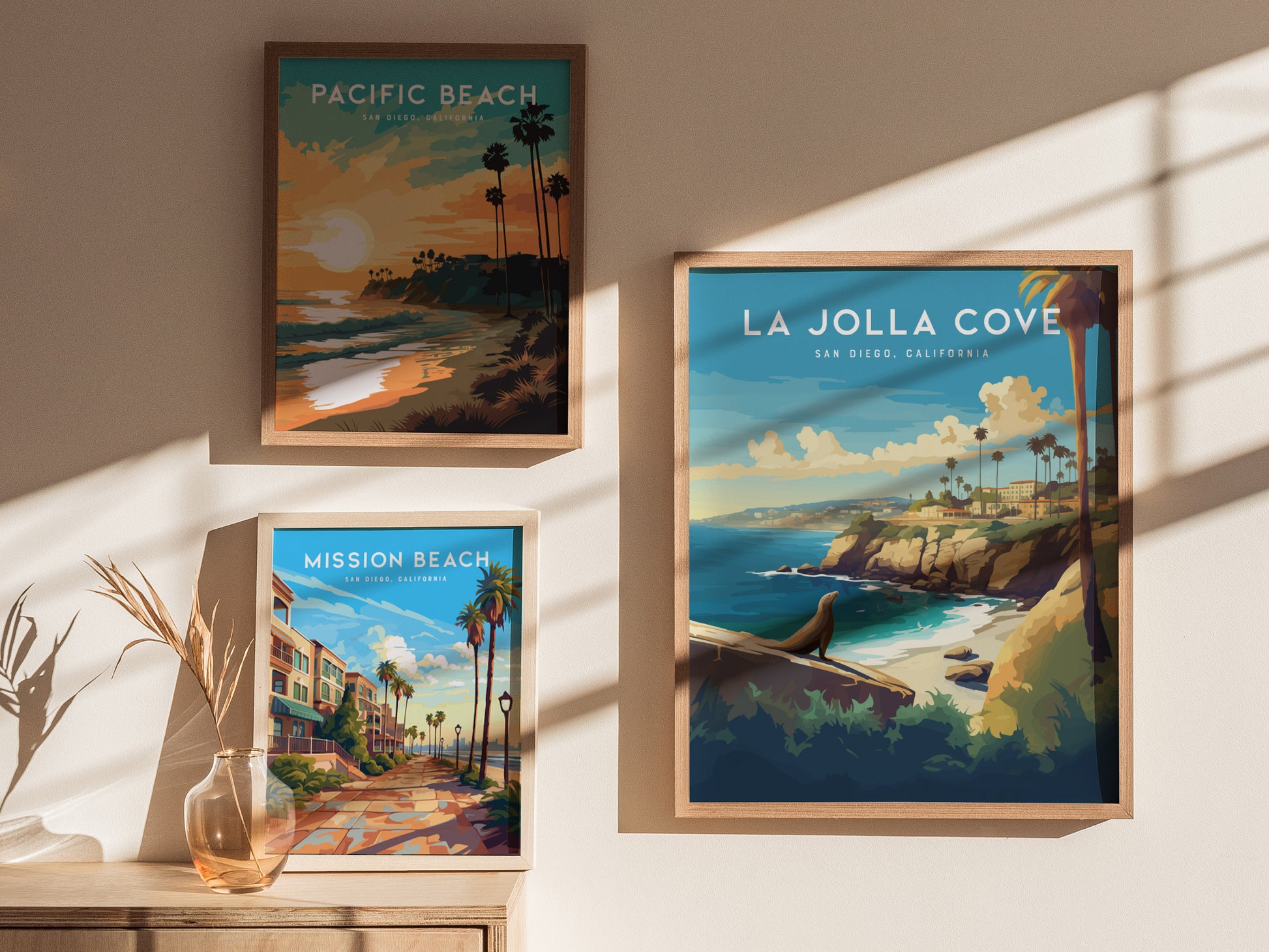 Three framed posters are displayed on a sunlit wall, featuring scenic illustrations of Pacific Beach, Mission Beach, and La Jolla Cove in San Diego, California, with coastal landscapes.