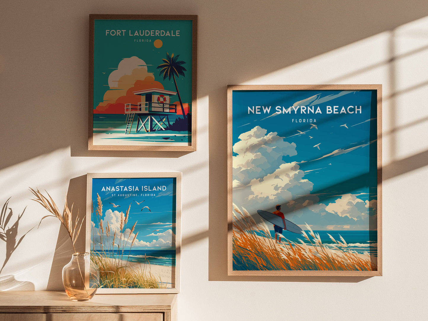 Three framed posters depict scenic Florida beaches: New Smyrna Beach with a surfer, Fort Lauderdale with a lifeguard hut, and Anastasia Island with seagulls. Sunlight casts shadows on the wall.