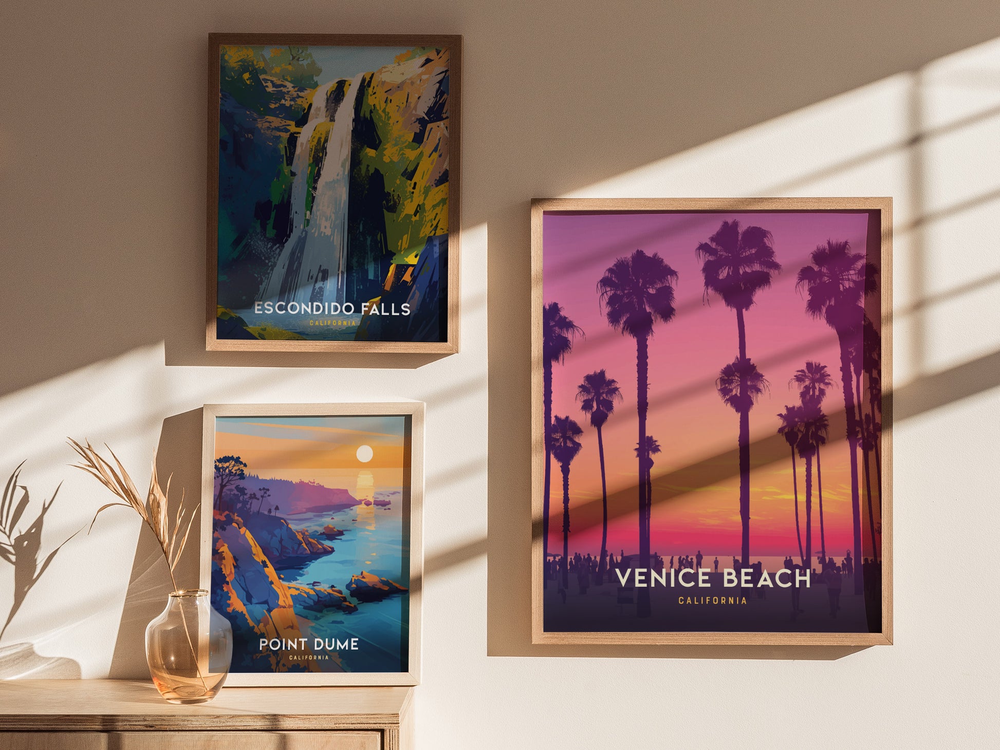 Three framed posters on a wall depict Escondido Falls, Point Dume, and Venice Beach. The Venice Beach poster features palm trees against a vibrant sunset. Shadows.