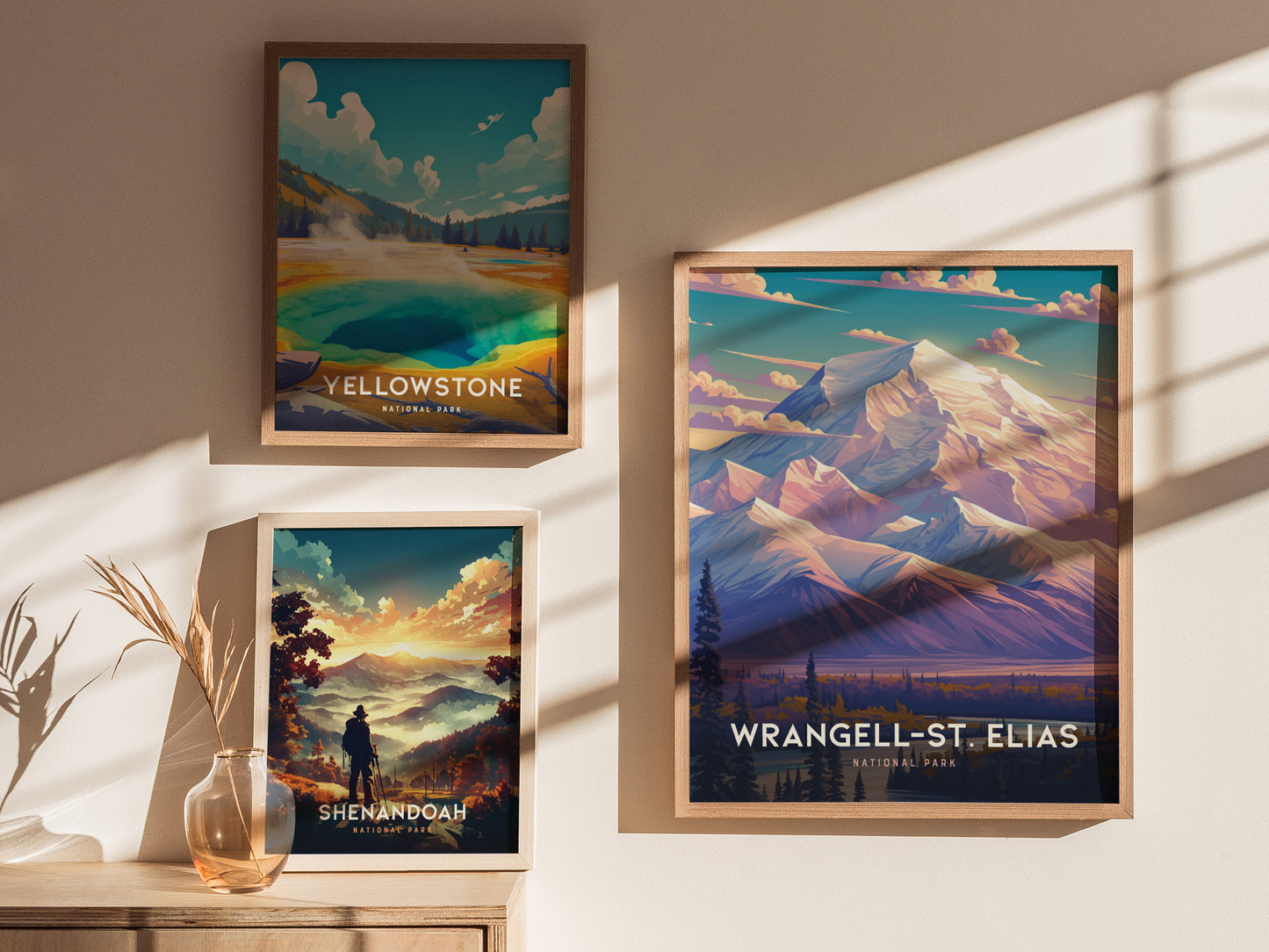Three framed posters hang on a beige wall, depicting Yellowstone, Shenandoah, and Wrangell-St. Elias National Parks. Sunlight casts shadows across the wall and a wooden table below.