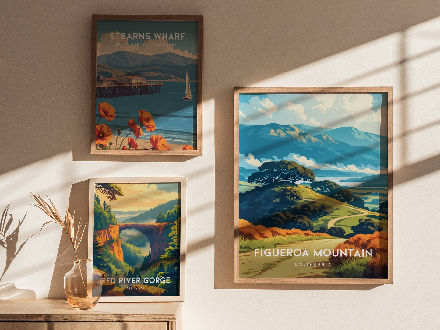 Three framed posters are displayed on a light-colored wall, showcasing scenic landscapes. The central poster features Figueroa Mountain in California, surrounded by rolling hills and vibrant greenery, while the other two depict.