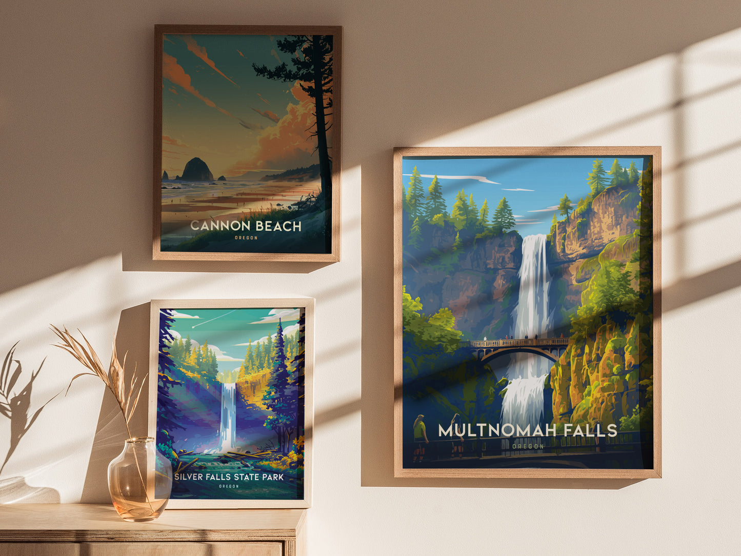 Three framed posters are displayed on a sunlit wall. They depict scenic landscapes: Cannon Beach, Silver Falls State Park, and Multnomah Falls, each featuring vibrant natural elements.