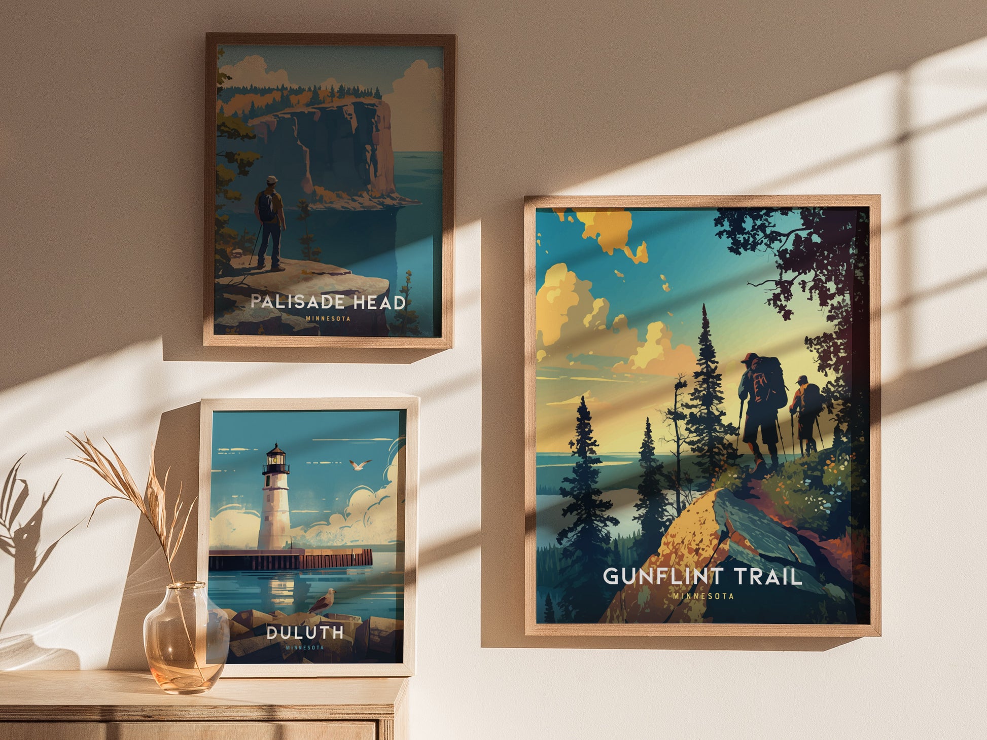 Three framed posters on a wall depict scenic landscapes: a hiker on Palisade Head, a lighthouse in Duluth, and two hikers on the Gunflint Trail. Soft sunlight casts shadows.