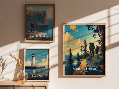 Three framed posters on a wall depict scenic landscapes: a hiker on Palisade Head, a lighthouse in Duluth, and two hikers on the Gunflint Trail. Soft sunlight casts shadows.