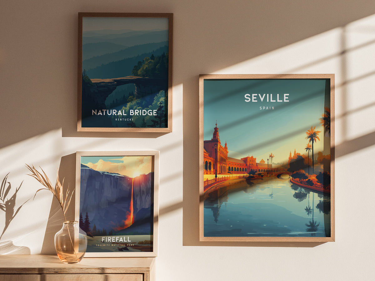 Three framed posters are displayed on a light-colored wall. The central poster features Seville, Spain with a vibrant sunset view of a river lined with palm trees and ornate buildings, while the others depict natural landscapes.