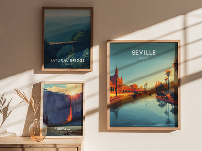 Three framed posters are displayed on a light-colored wall. The central poster features Seville, Spain with a vibrant sunset view of a river lined with palm trees and ornate buildings, while the others depict natural landscapes.