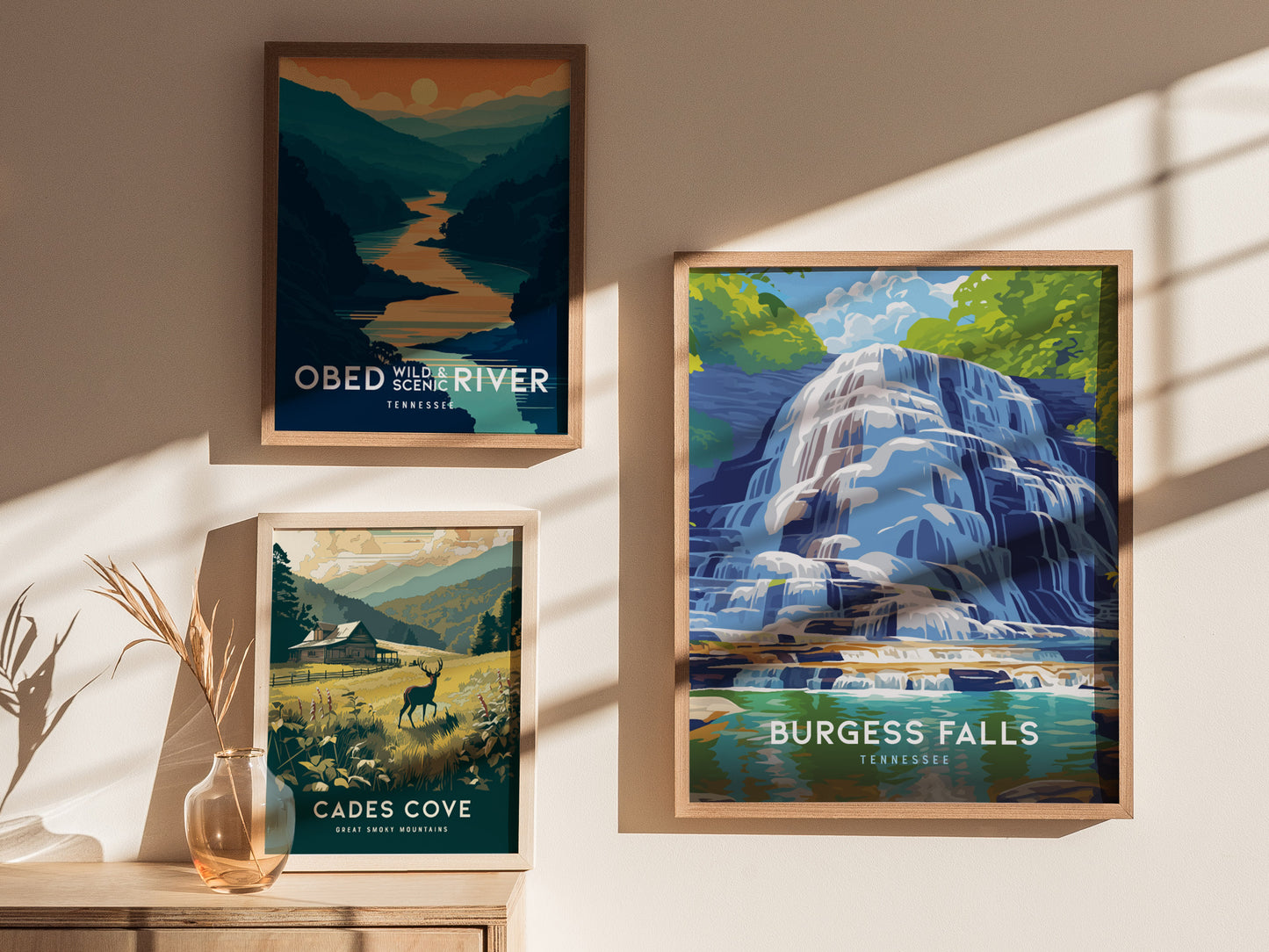 Three framed art prints are displayed on a wall, depicting Obed Wild & Scenic River, Cades Cove, and Burgess Falls, with sunlight casting shadows across them.