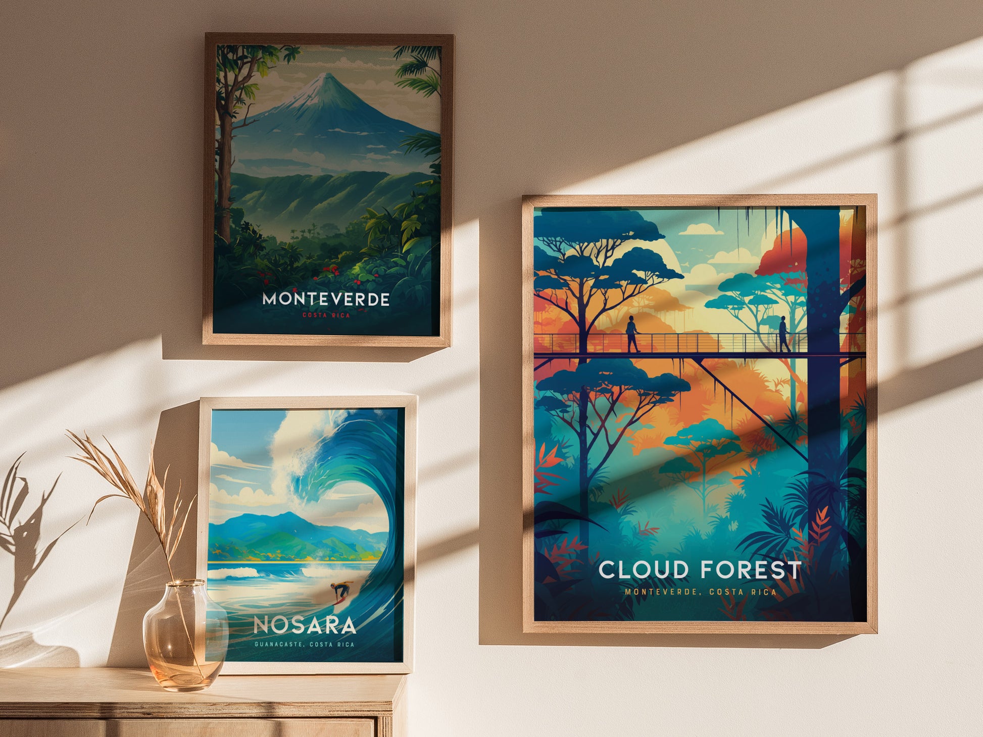 Three framed posters are displayed on a wall, featuring colorful illustrations of Monteverde, Nosara, and a cloud forest canopy walkway. Sunlight casts shadows across the wall.