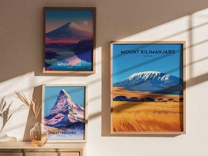 Three framed posters on a sunlit wall depict Mount Fuji, Mount Kilimanjaro, and the Matterhorn, each showcasing vibrant landscapes and iconic peaks. A decorative vase with dry plants sits below.