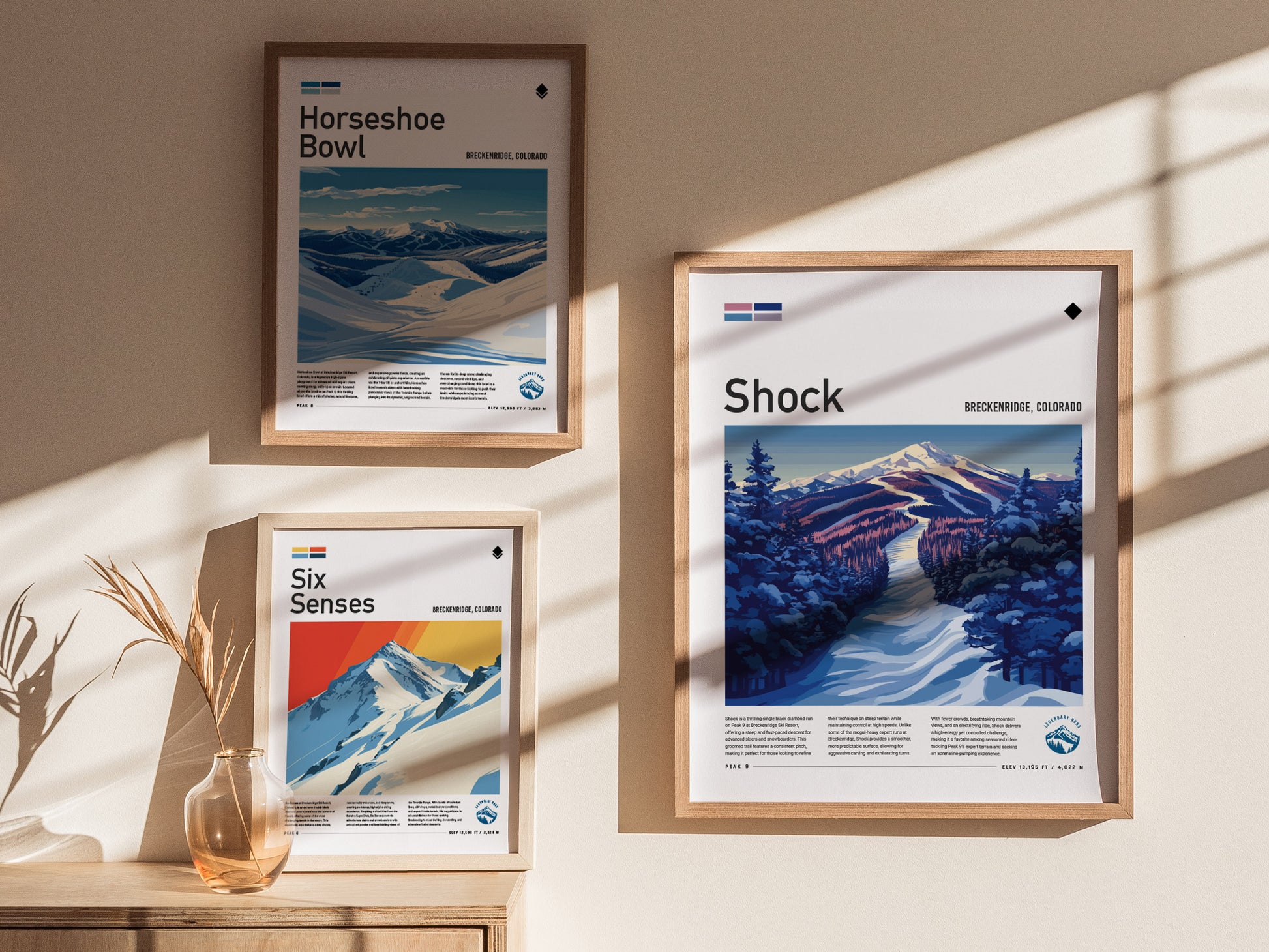 Three framed posters on a wall depict ski art from Breckenridge, Colorado, including Horseshoe Bowl, Six Senses, and Shock, with sunlight casting shadows.