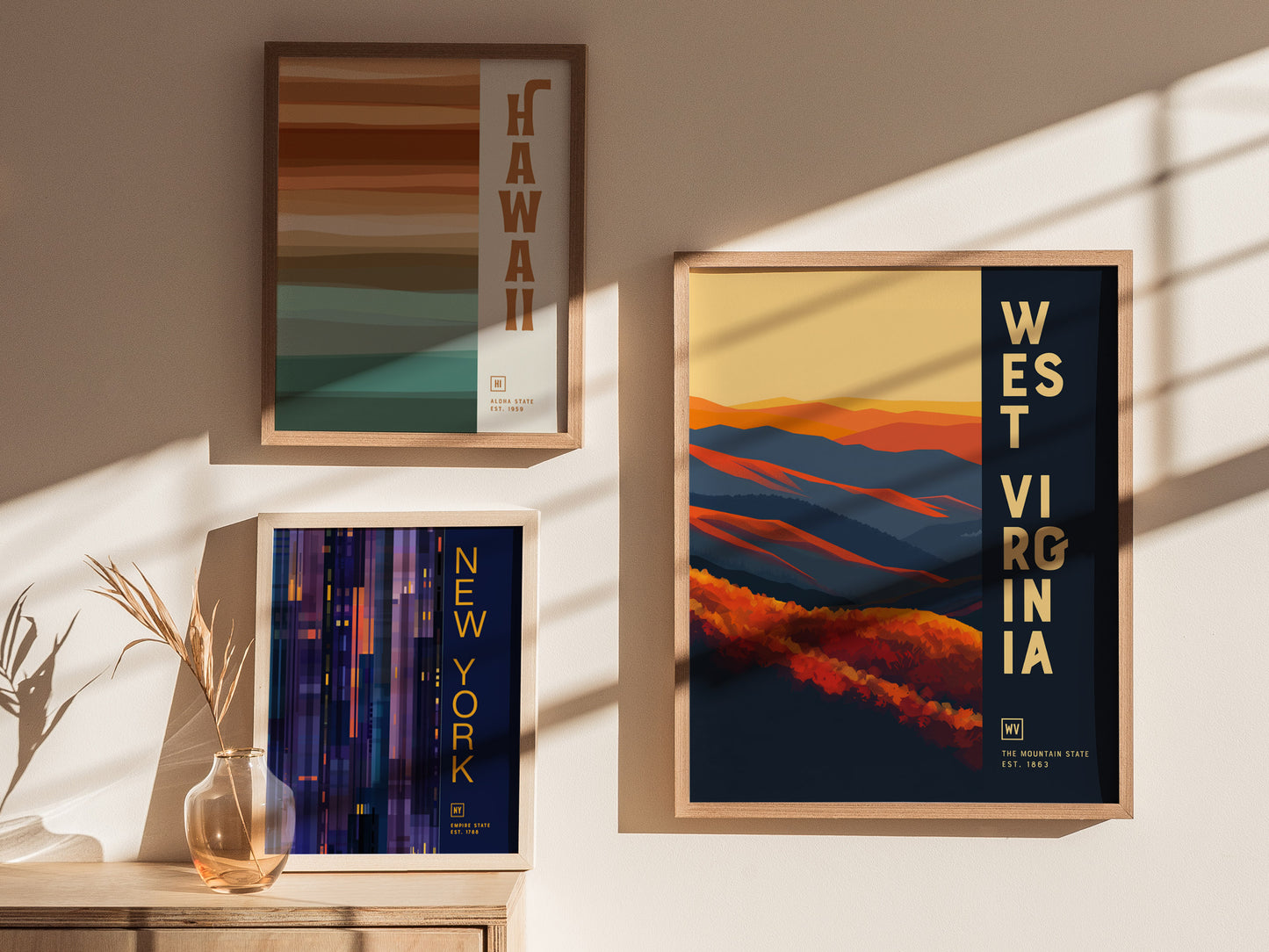 Three framed posters are displayed on a wall: one for Hawaii with earthy stripes, one for New York in vertical lines, and one for West Virginia with colorful hills.