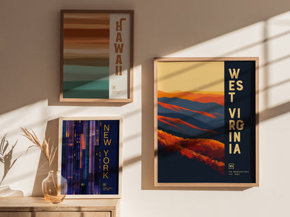 Three framed posters are displayed on a wall: one for Hawaii with earthy stripes, one for New York in vertical lines, and one for West Virginia with colorful hills.