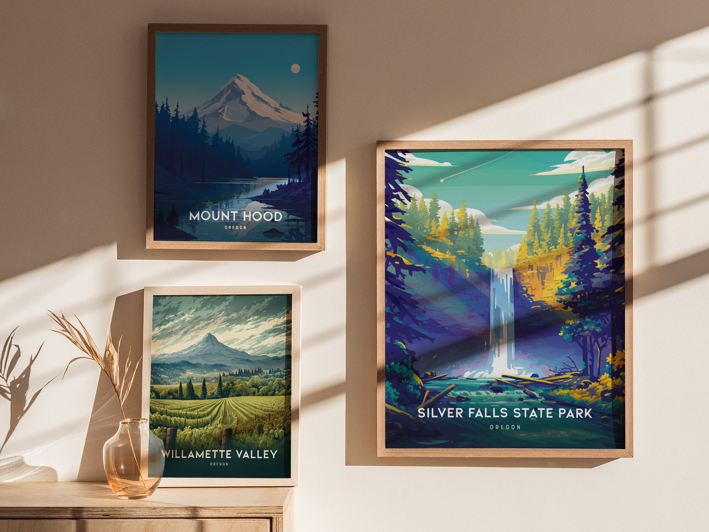 Three framed posters on a sunlit wall feature Mount Hood, Willamette Valley, and Silver Falls State Park, each depicting scenic Oregon landscapes with mountains and waterfalls.