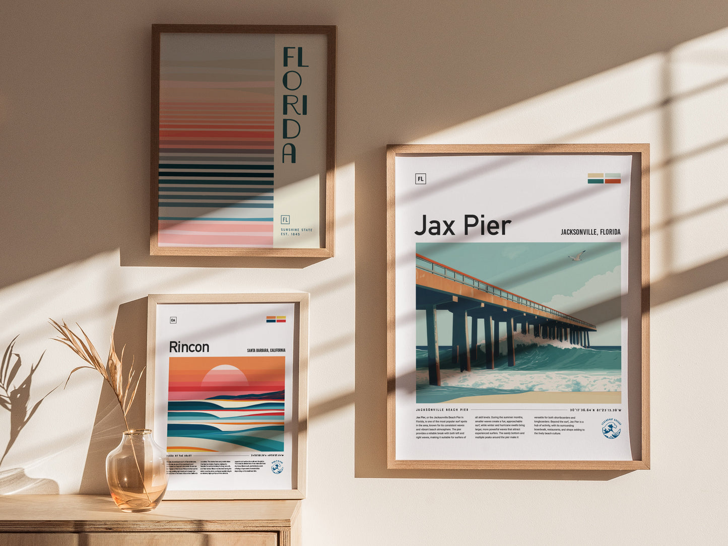 Three framed art posters are displayed on a wall, featuring abstract designs and scenes from Florida and California, with sunlight casting shadows on the wall.