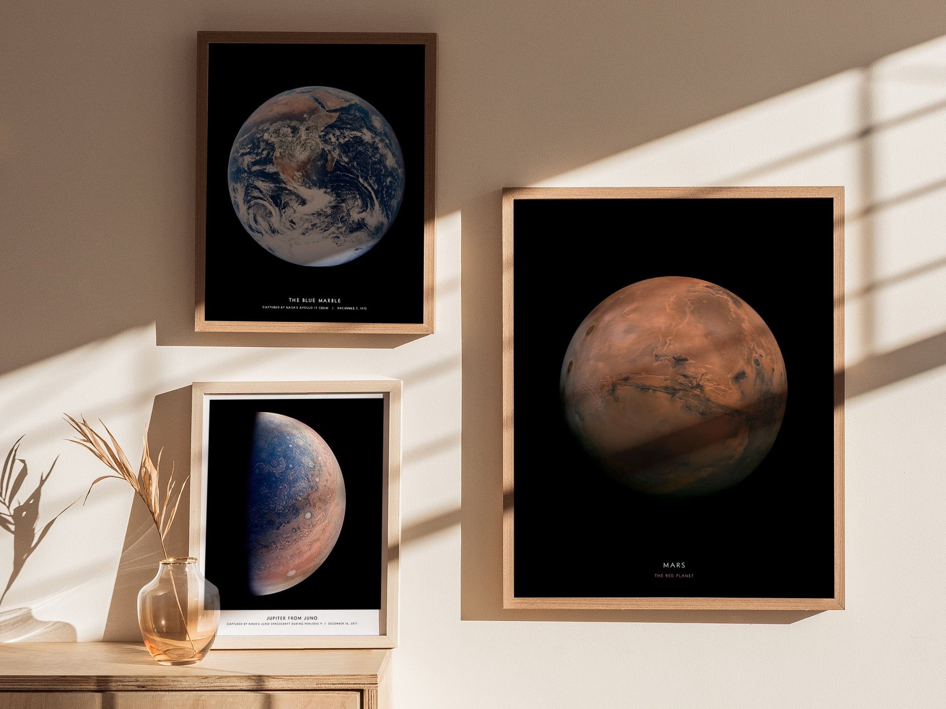 Framed posters of Earth and Mars on a wall with sunlight casting shadows.