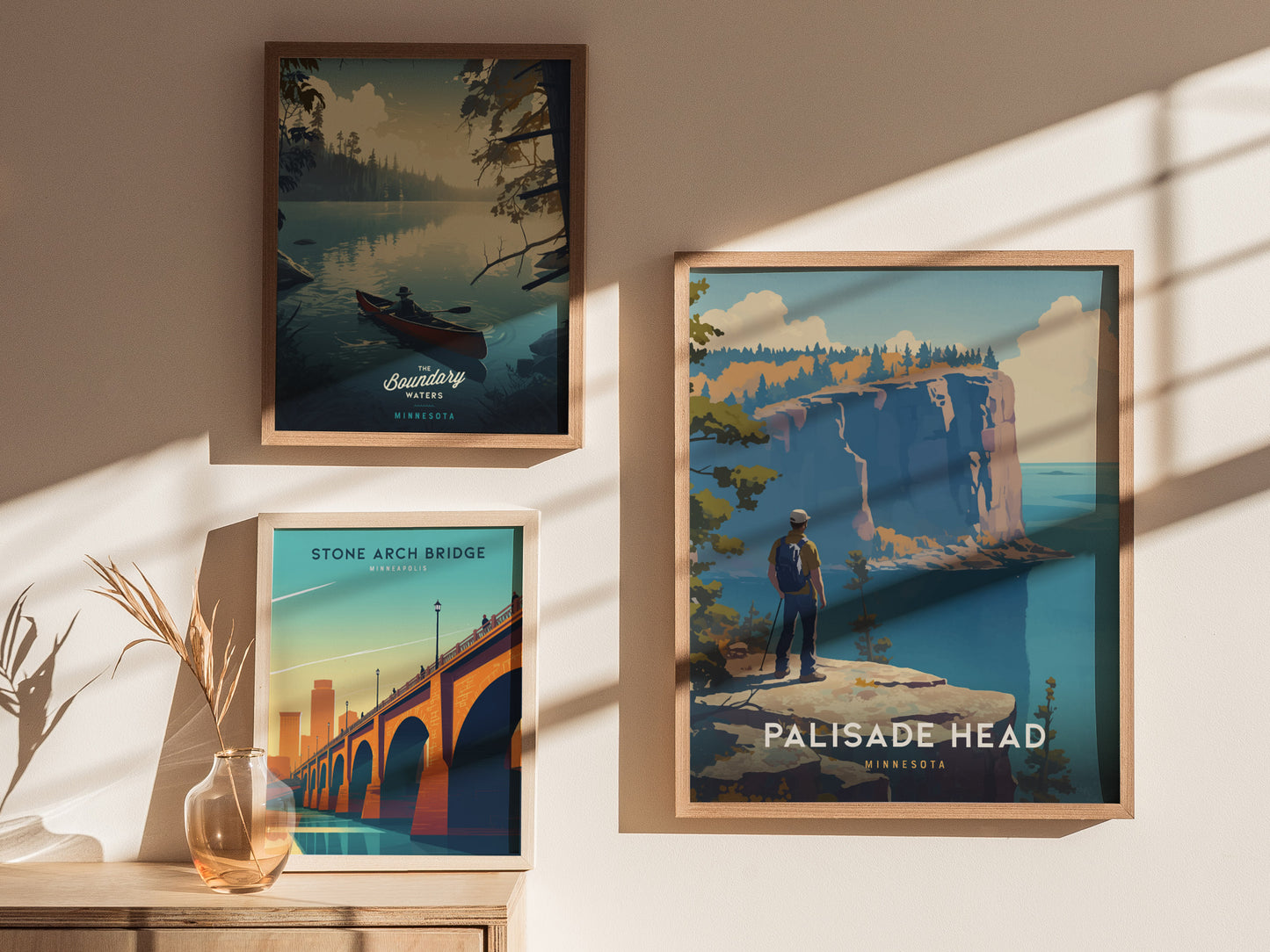 Three framed posters are displayed on a sunlit wall. They depict Minnesotas Boundary Waters, Stone Arch Bridge, and Palisade Head, with vibrant landscapes and natural themes.