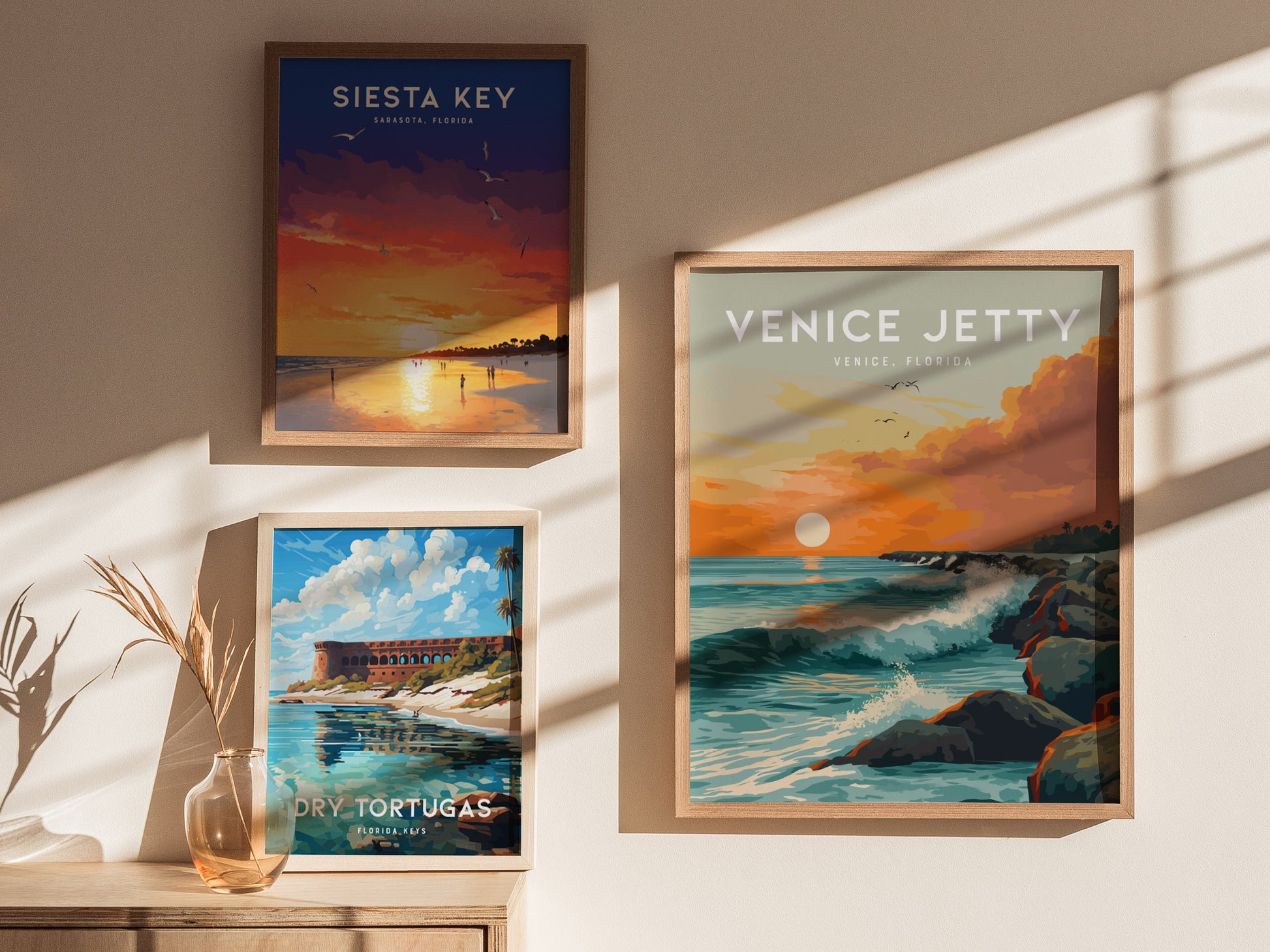 Three framed posters are displayed on a sunlit wall. They depict Siesta Keys sunset, the Venice Jetty with waves, and Dry Tortugas with a historic fort and clear skies.
