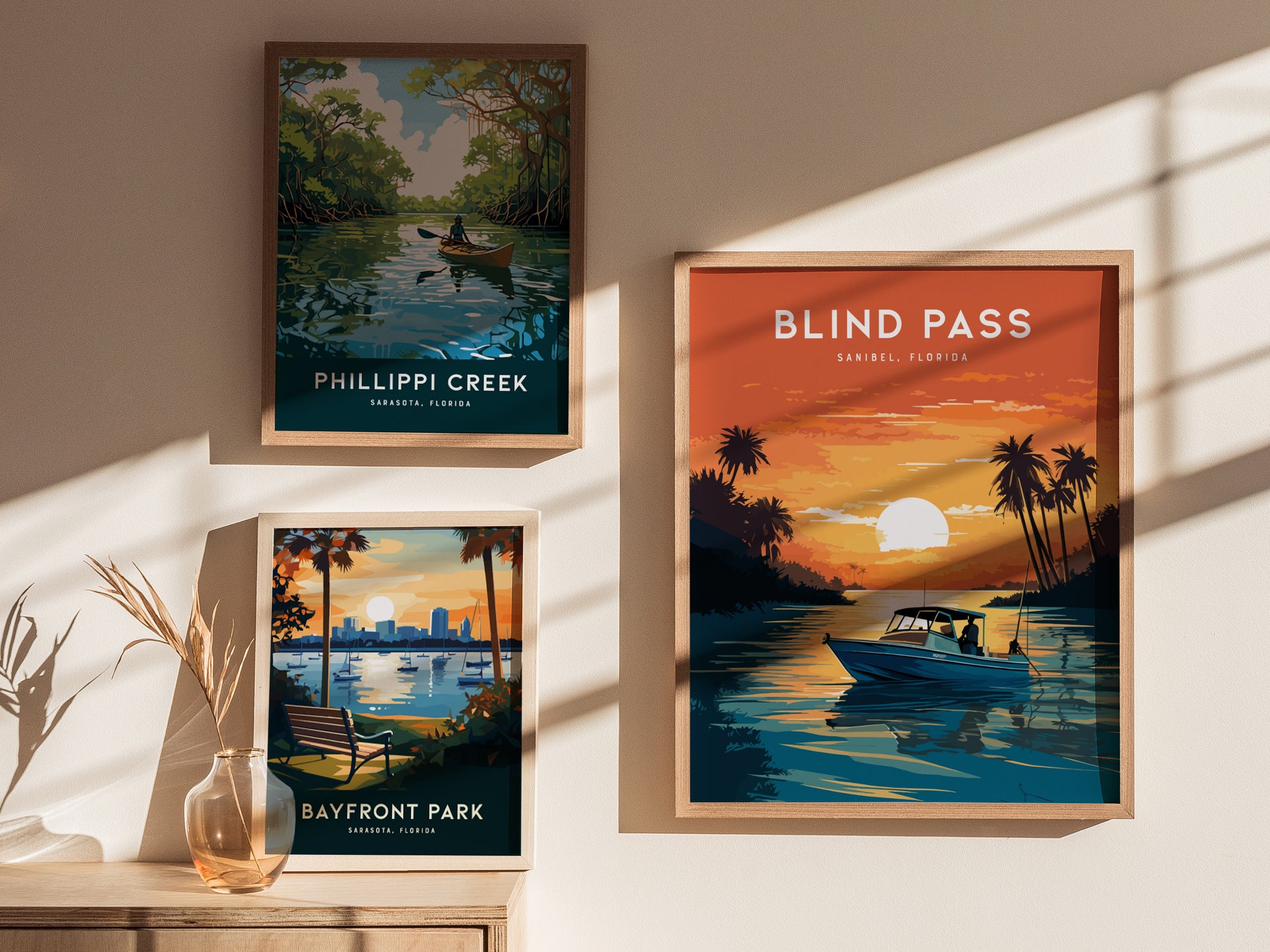 Three framed posters are displayed on a wall, featuring scenic illustrations of Phillippi Creek, Bayfront Park, and Blind Pass with vibrant colors and natural landscapes.