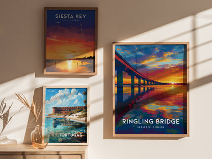 Three framed posters hang on a sunlit wall. The largest shows a vibrant sunset over the Ringling Bridge, reflecting in the water. The others depict a sunset at Siesta Key and a scenic view of Dry Tortugas with bright skies.