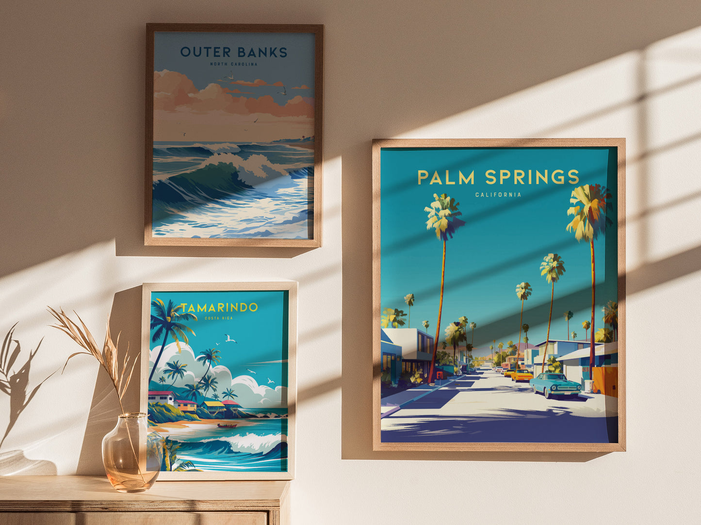 Three framed posters are displayed on a wall, featuring vibrant scenes from Palm Springs, Outer Banks, and Tamarindo, each showcasing palm trees and coastal landscapes.