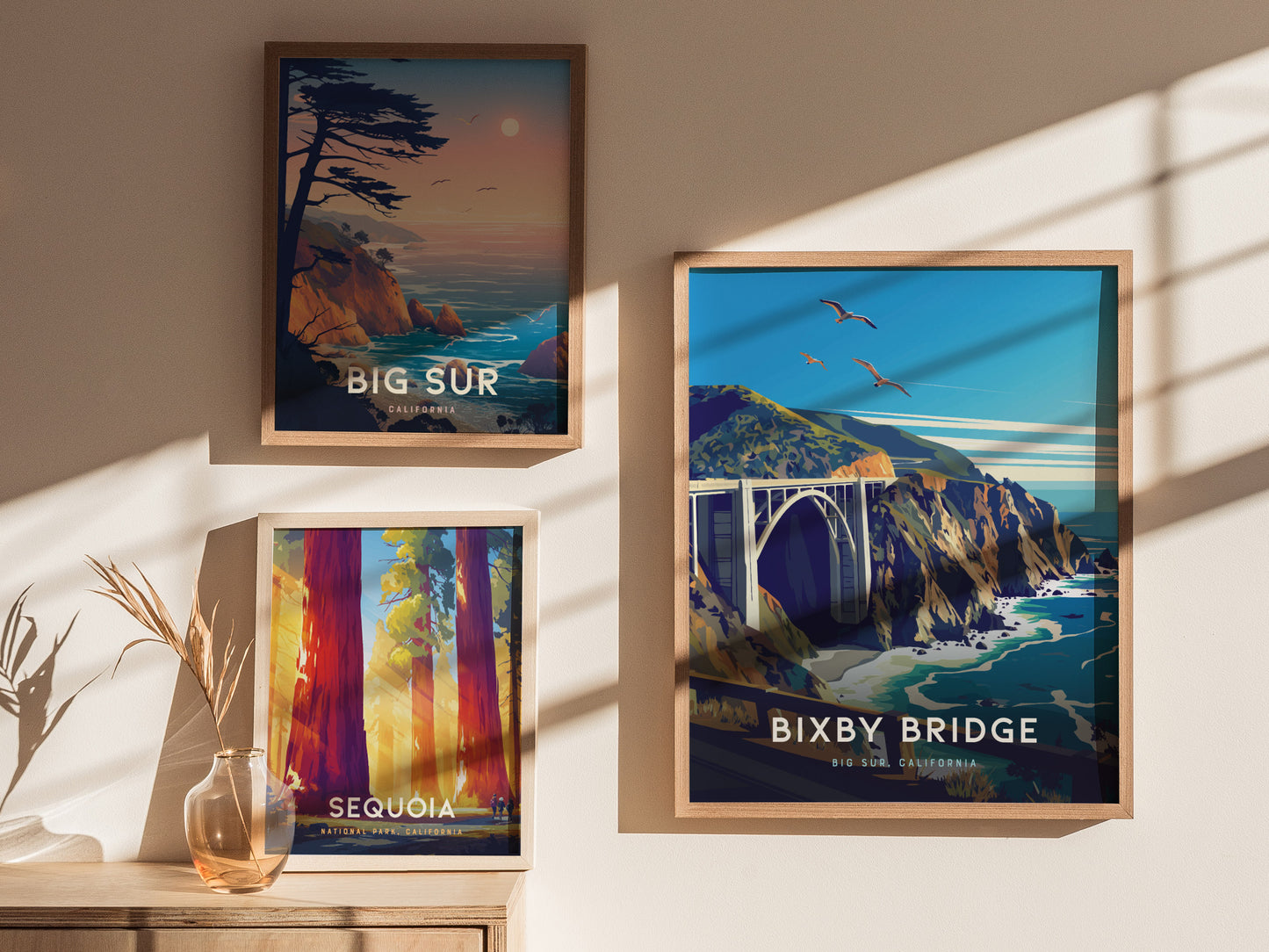Three framed posters are displayed on a wall: one of Bixby Bridge in Big Sur, another of a coastal sunset, and a third featuring Sequoia trees.