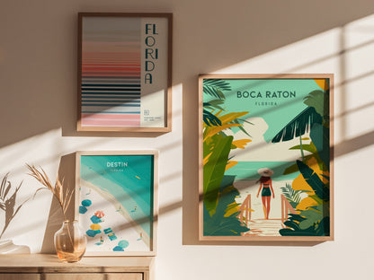 Three framed travel prints are displayed on a sunlit wall, featuring Boca Raton, Destin, and a Florida design with colorful stripes. A vase with dried grass is nearby.