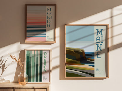 Three framed posters on a sunlit wall, featuring minimalist designs labeled Florida, Maine, and Oregon, with abstract landscapes in warm.