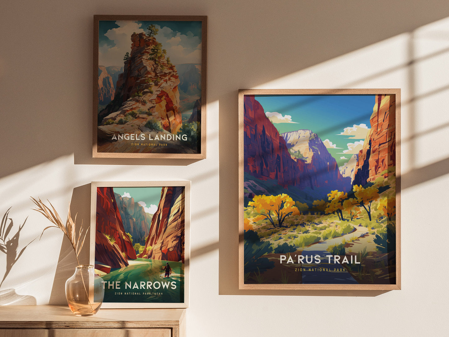 Three framed posters of Zion National Park landscapes are displayed on a wall, featuring Angels Landing, The Narrows, and Parus Trail, with sunlight casting shadows.