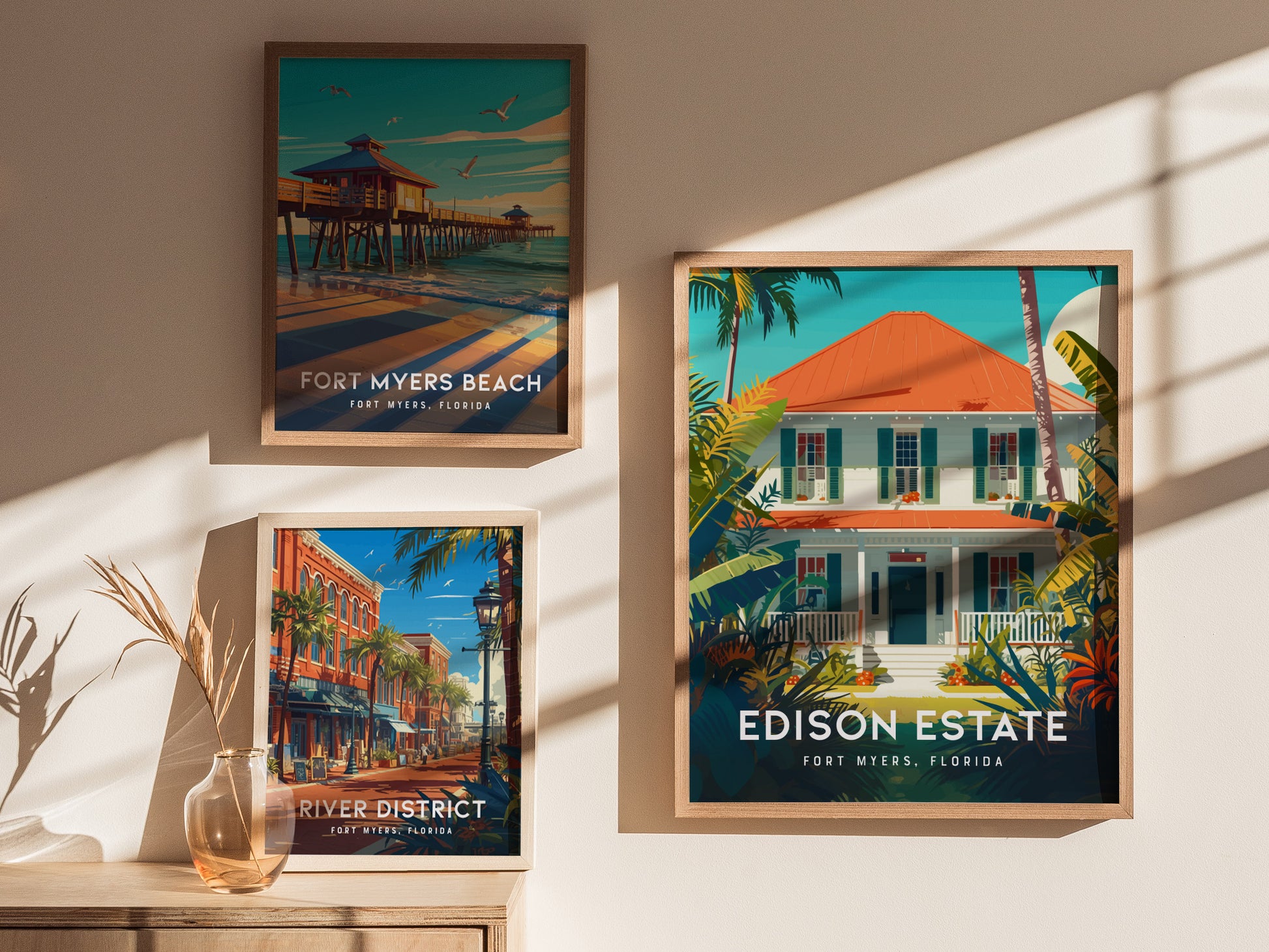 Three framed posters on a wall depict Fort Myers Beach, the River District, and Edison Estate in vibrant colors, with sunlight casting shadows across them.