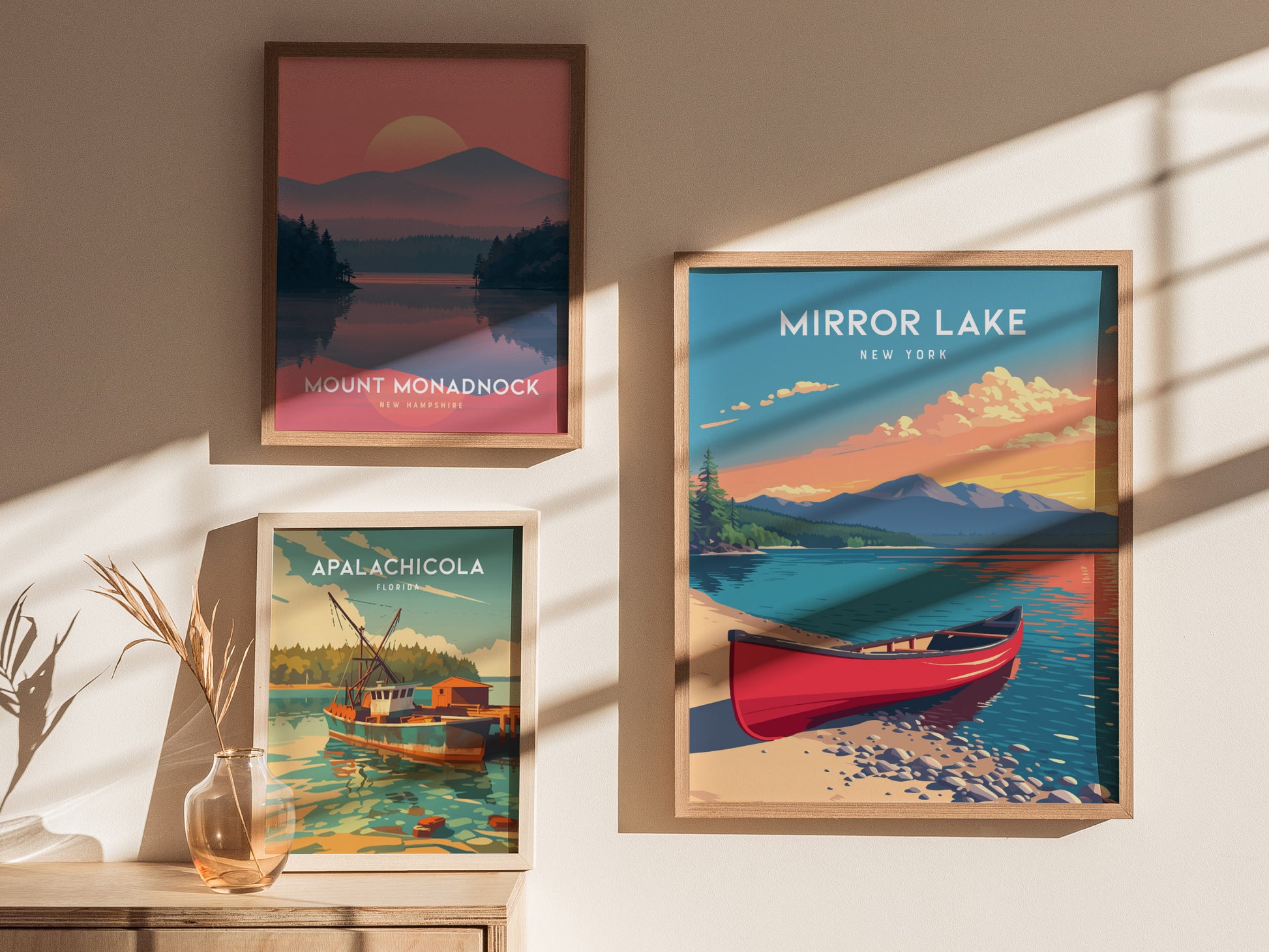 Three framed posters are displayed on a light-colored wall, featuring scenic landscapes. The left poster depicts Mount Monadnock, the center poster showcases Mirror Lake, New York with a red canoe, and the right poster highlights.