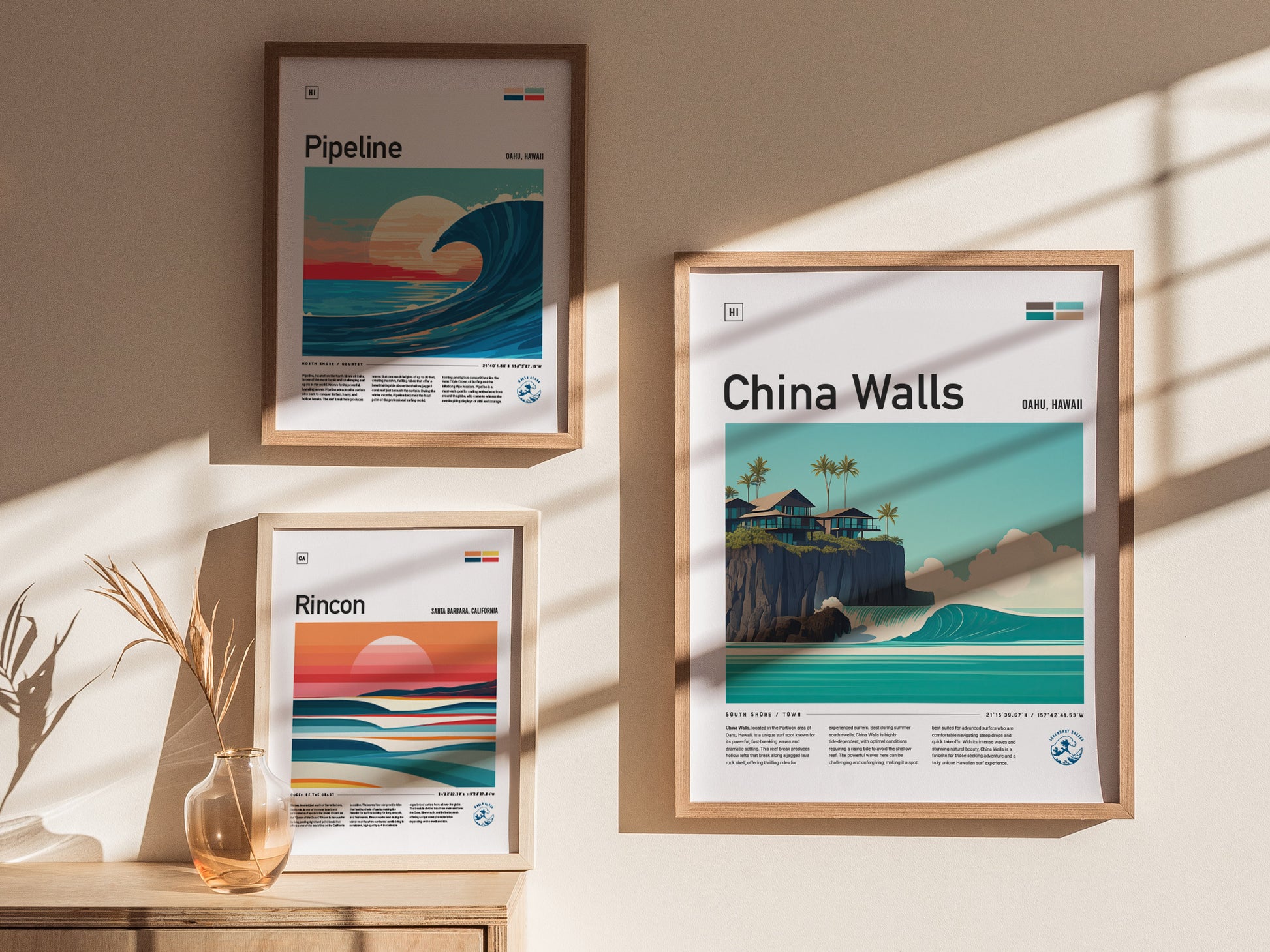 Three framed posters hang on a sunlit wall, depicting surf spots: Pipeline, Rincon, and China Walls, each showcasing vibrant waves and coastal scenery. A vase with dried plants sits below.