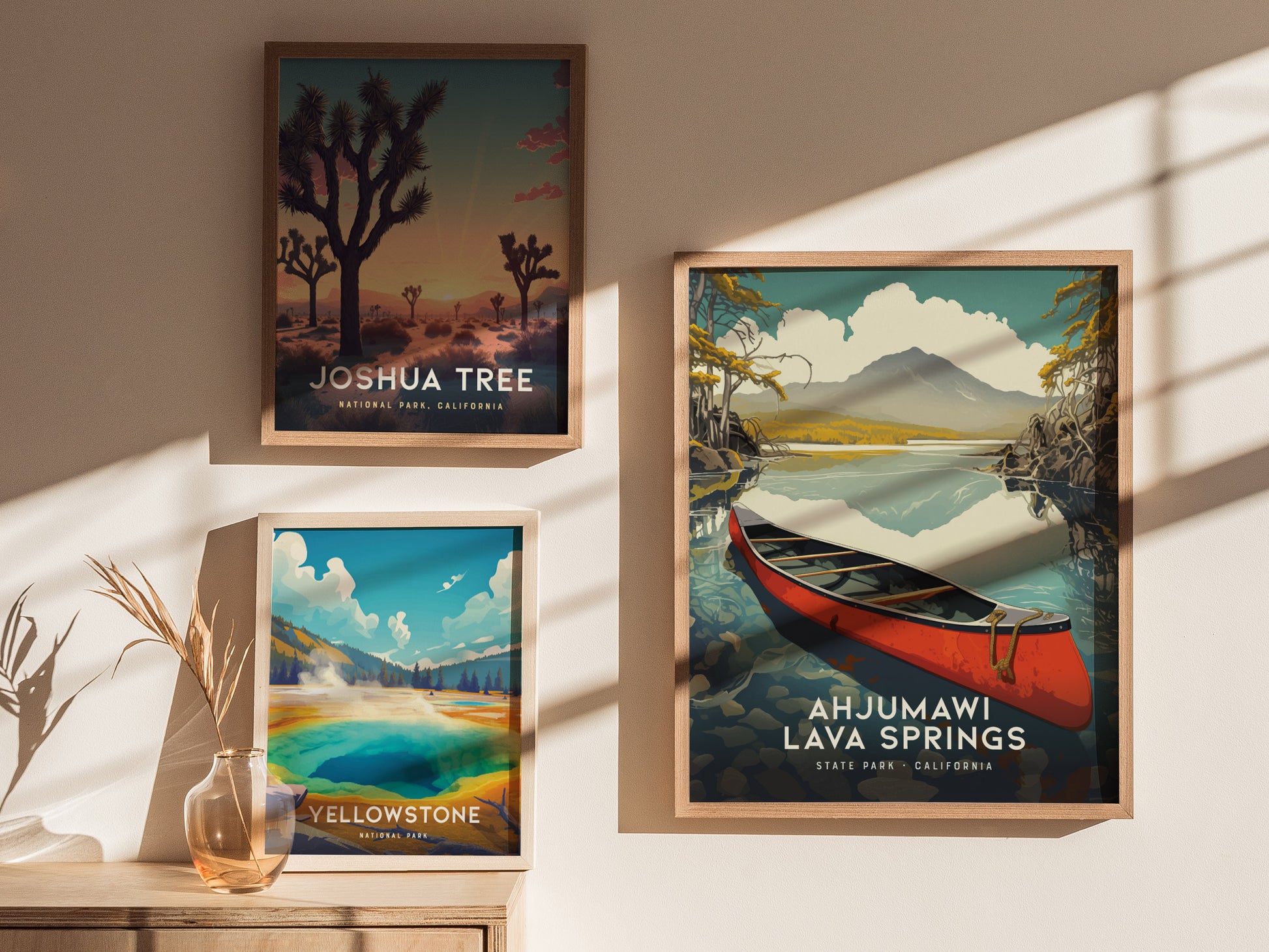Three framed posters display scenic artwork of Joshua Tree, Yellowstone, and Ahjumawi Lava Springs with a red canoe. Sunlight casts shadows on the wall and wooden surface.