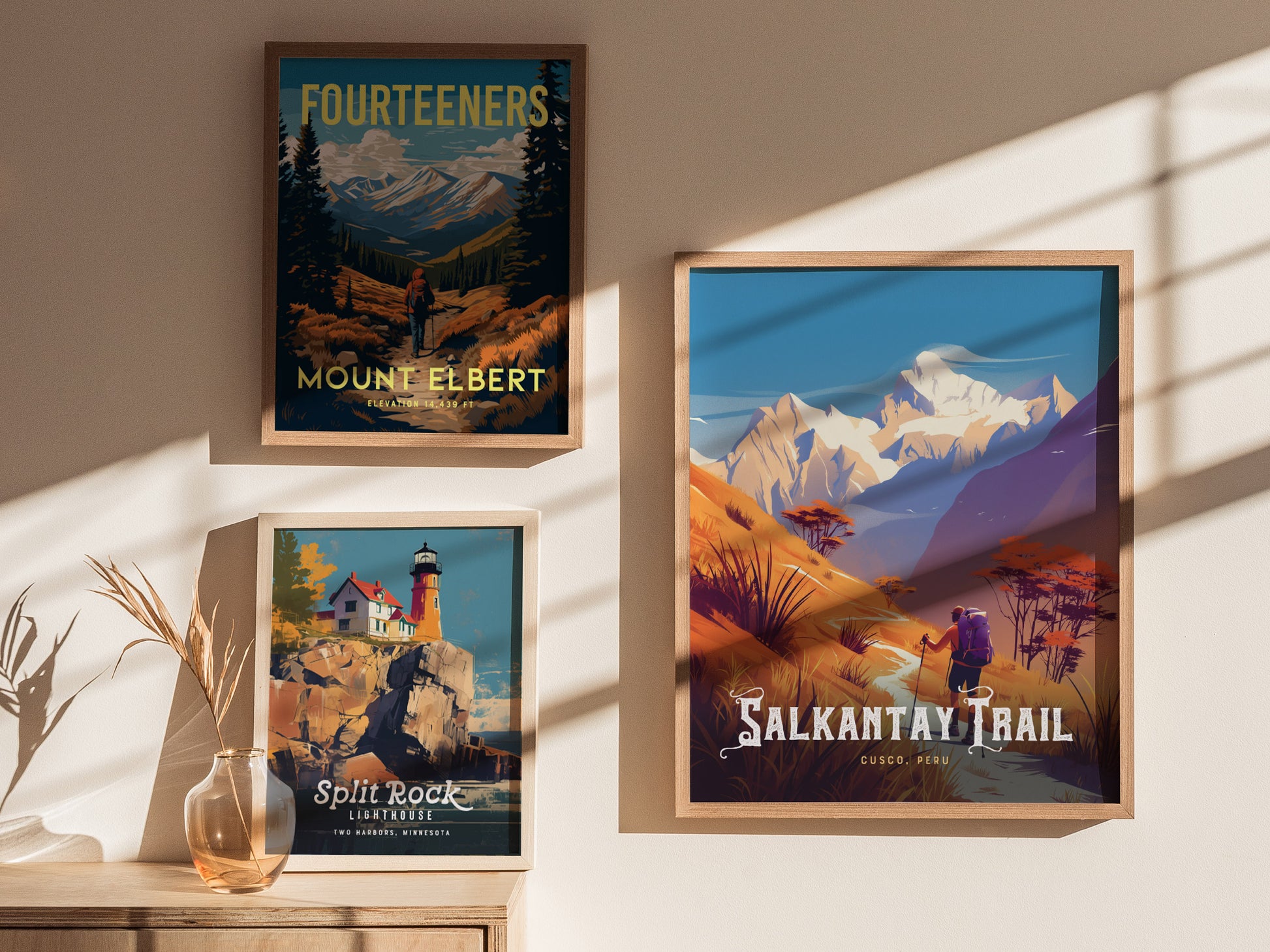 Three framed posters are displayed on a sunlit wall, featuring Mount Elbert, Split Rock Lighthouse, and the Salkantay Trail with vibrant landscapes and colorful illustrations.